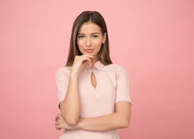 Portrait of a young woman posing elegantly in a studio with a pink background.
